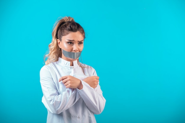 Female doctor in white uniform covering her mouth and crossing her arms. 