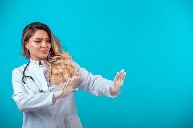 Female doctor in white uniform stopping something ahead. 