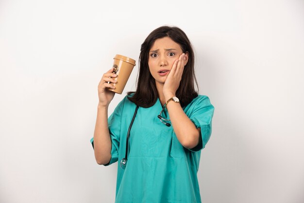 白い背景に彼女の頬を保持しているコーヒーのカップを持つ女性医師。