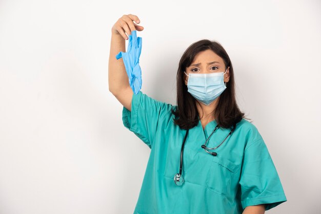 Женщина-врач с маской, держащей перчатки на белом фоне. Фото высокого качества