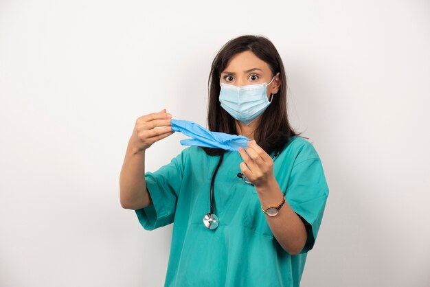 Female doctor with medical mask holding gloves on white background.