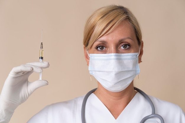 Free photo female doctor with medical mask holding vaccine syringe
