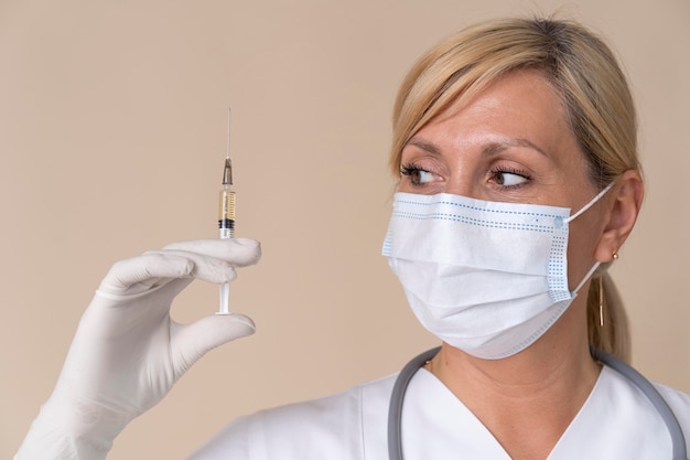 Female doctor with medical mask holding vaccine syringe