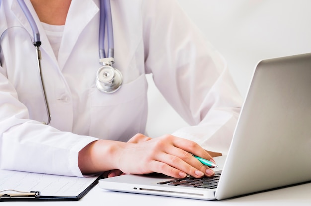 A female doctor with stethoscope around her neck using laptop on desk