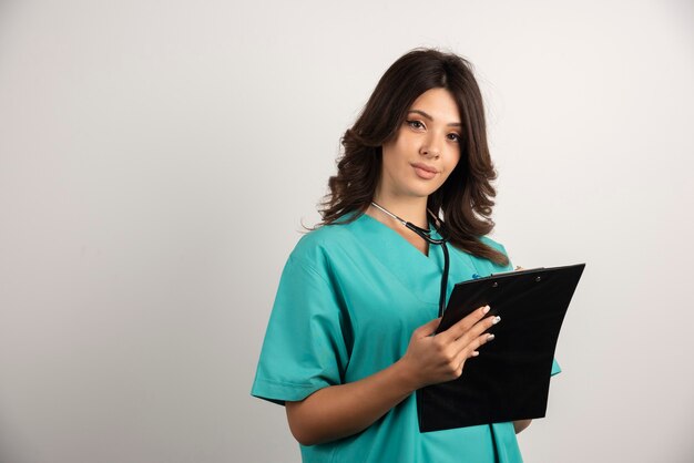 Female doctor with stethoscope and clipboard looking at camera.