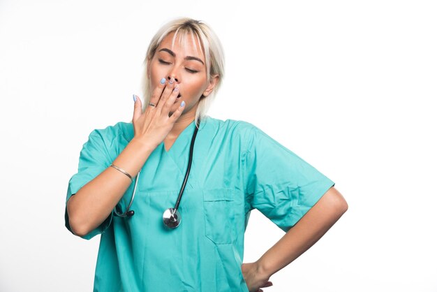 Female doctor with stethoscope feeling sleepy on white surface