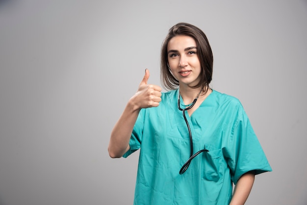 Женщина-врач со стетоскопом дает большие пальцы руки вверх. Фото высокого качества