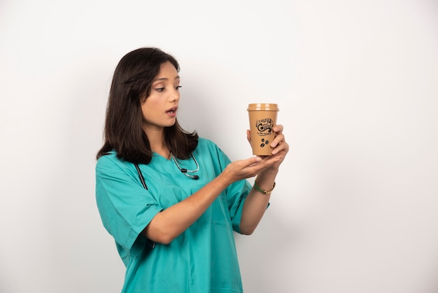 Female doctor with stethoscope looking at coffee on white background.