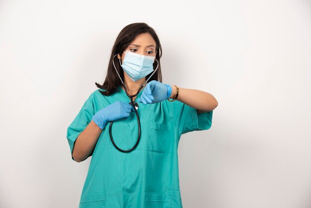 Female doctor with stethoscope and mask checking time on white background. High quality photo