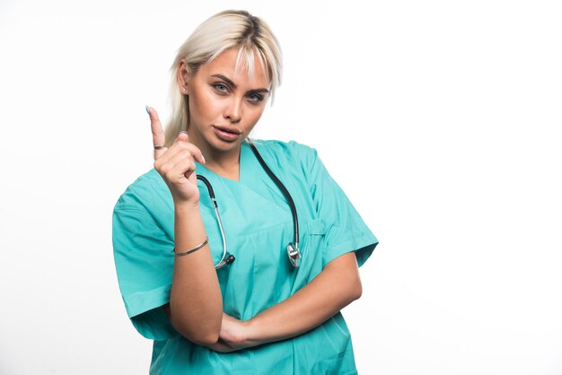 Female doctor with stethoscope pointing finger on white surface