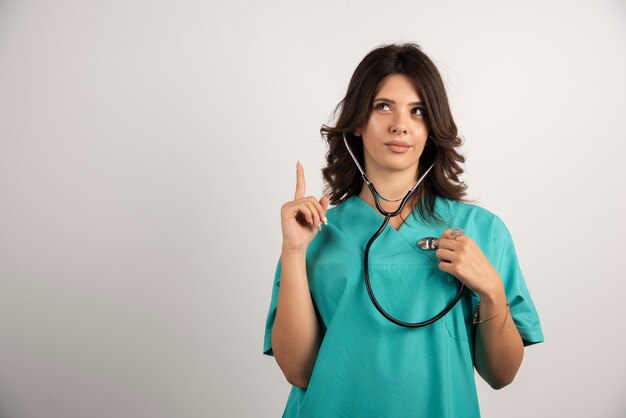 Female doctor with stethoscope pointing at upside.