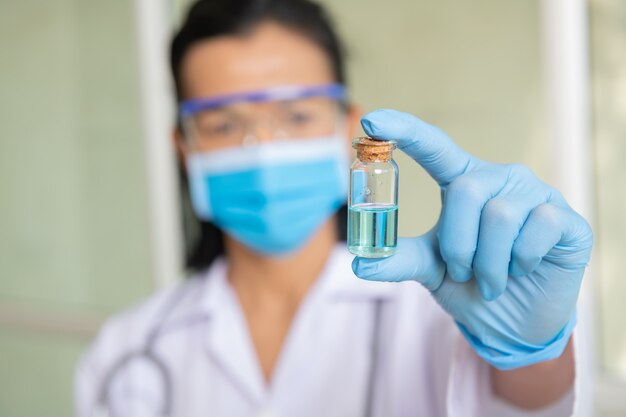 Female doctor with a stethoscope on shoulder holding syringe and COVID-19 vaccine. Coronavirus Vaccine concept in hand of doctor blue vaccine jar. Vaccine Concept of fight against coronavirus.