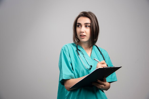 Female doctor with stethoscope writing on clipboard. 