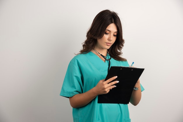Женщина-врач со стетоскопом писать на доске сзажимом для бумаги.