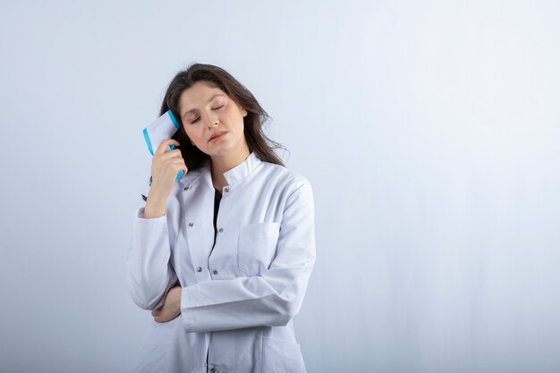 female doctor with thermometer standing on white wall. 