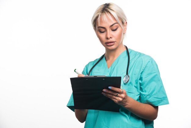 Female doctor writing something on clipboard with pen on white surface