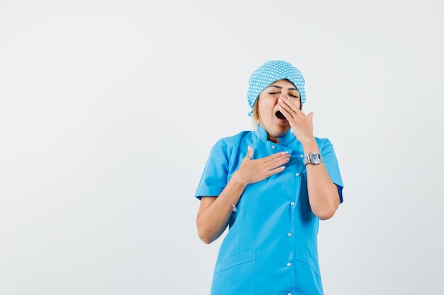 Женщина-врач зевает в синей форме и выглядит сонной
