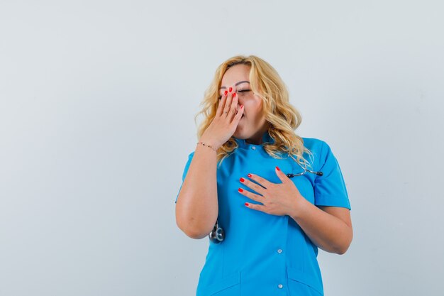 Female doctor yawning with hand on mouth in blue uniform and looking sleepy space for text