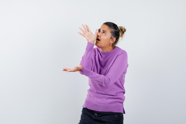 Female doing funny gesture with hand on nose in wool blouse and looking focused 