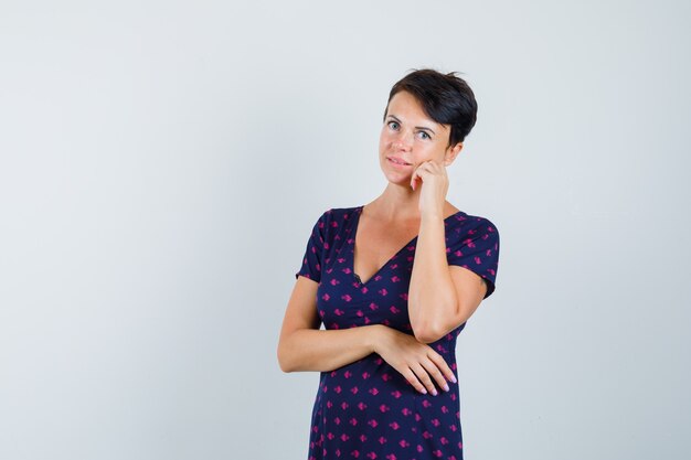 Female in dress standing in thinking pose and looking sensible , front view.