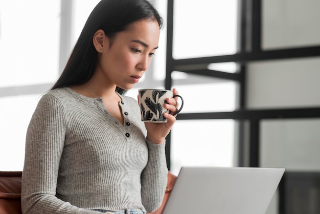 Free photo female drinking tea and using laptop