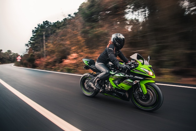 A female driver driving green neon color motorcycle on the road.