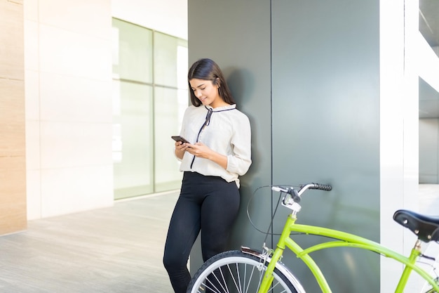 Female employee using mobile applications by green bicycle against column