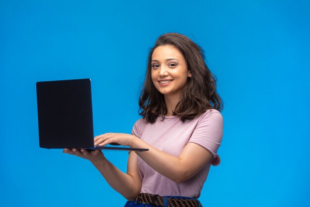 Female employee with a black laptop having video call while looking to the camera.