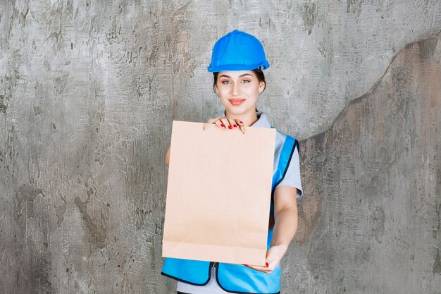 Женский инженер в синем шлеме и шестерне, держа картонную хозяйственную сумку.