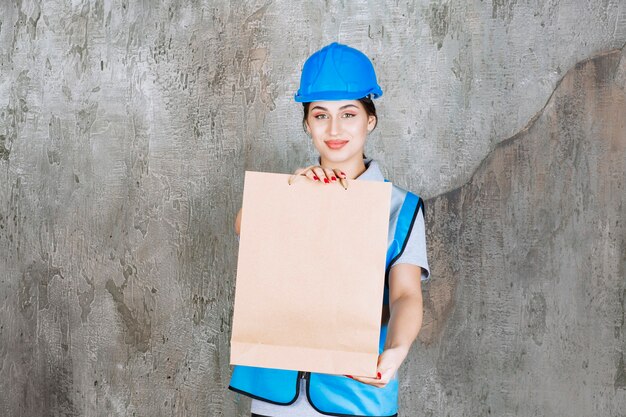 Female engineer in blue helmet and gear holding a cardboard shopping bag. 