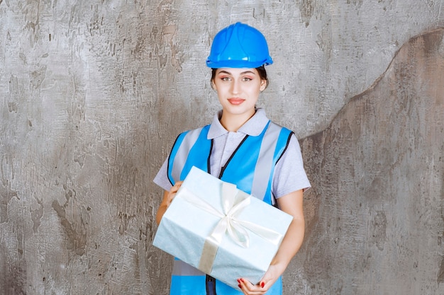 Female engineer in blue uniform and helmet holding a blue gift box.