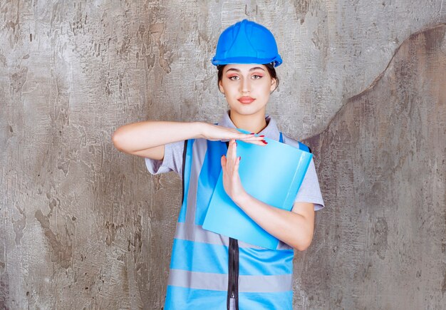 파란색 제복을 입은 여성 엔지니어와 파란색 보고서 폴더를 들고 있는 헬멧