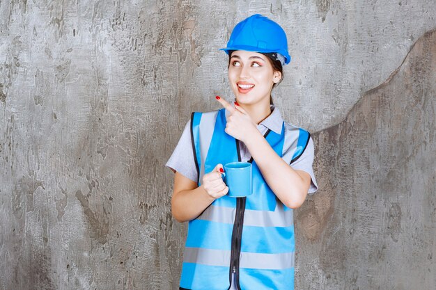 Female engineer in blue uniform and helmet holding a blue tea cup. 