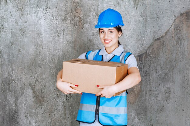 Female engineer in blue uniform and helmet holding a cardboard parcel.