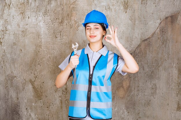 Female engineer in blue uniform and helmet holding a metallic wrench.