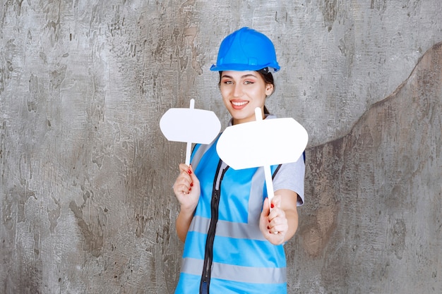 Free photo female engineer in blue uniform and helmet holding two blank info boards in both hands