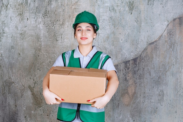 Female engineer in green helmet holding a cardboard box.