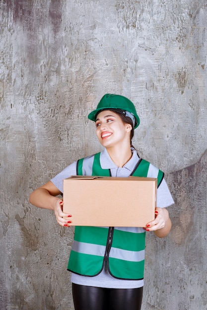 Ingegnere donna in casco verde che tiene una scatola di cartone