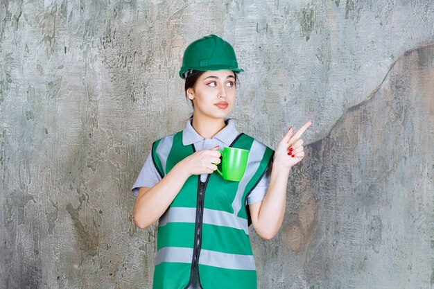 Female engineer in green helmet holding a green coffee mug.