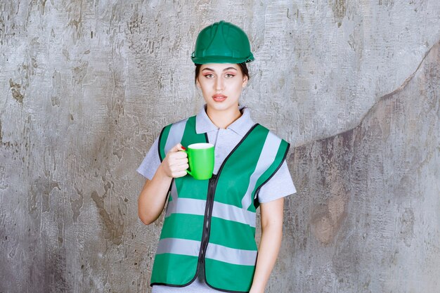 녹색 커피잔을 들고 녹색 헬멧에 여성 엔지니어