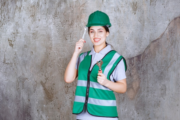 Free photo female engineer in green helmet holding metallic wrench for a repair work and looks confused and thoughtful.