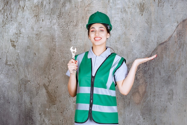 Female engineer in green helmet holding metallic wrench for a repair work