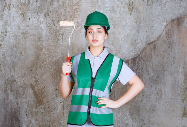 Женщина-инженер в зеленом шлеме держит обрезной валик для росписи стен