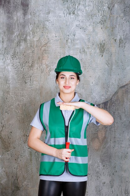 벽화를 위한 트림 롤러를 들고 녹색 헬멧을 쓴 여성 엔지니어