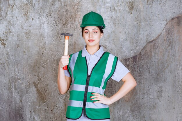 Female engineer in green helmet holding a wooden handled ax for a repair work