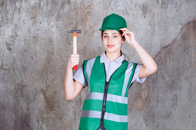 수리 작업을 위해 나무로 된 도끼를 들고 녹색 헬멧을 쓴 여성 엔지니어
