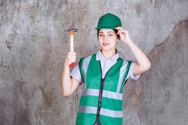 Женщина-инженер в зеленом шлеме держит топор с деревянной ручкой для ремонтных работ