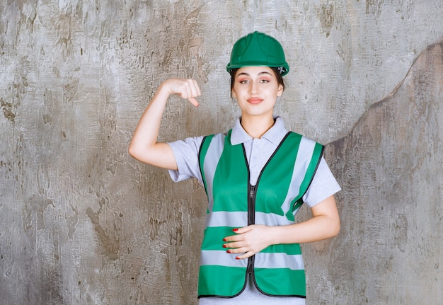 Женский инженер в зеленой форме и шлеме, демонстрируя мышцы руки.