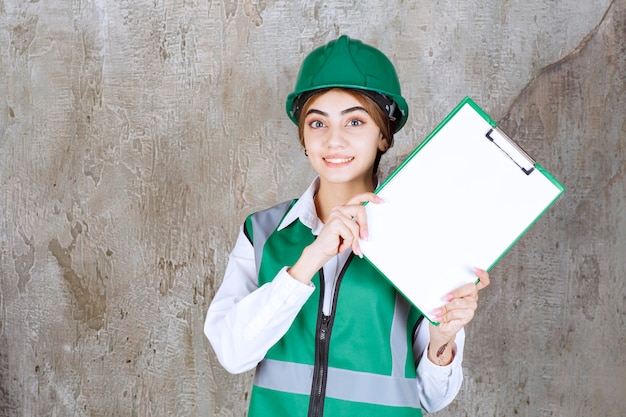 Foto gratuita ingegnere femminile in uniforme verde e casco che dimostra l'elenco dei progetti