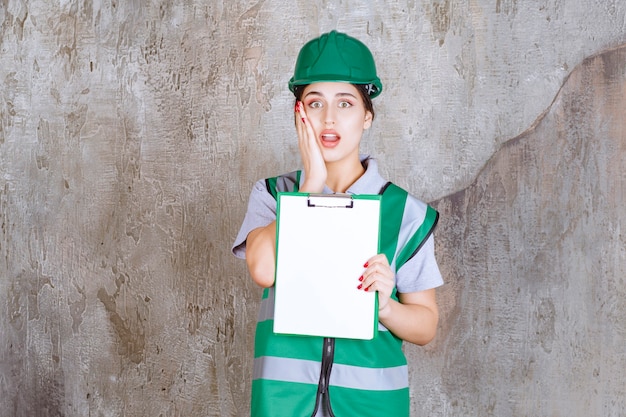 Female engineer in green uniform and helmet demonstrating the project sheet and looks terrified and scared